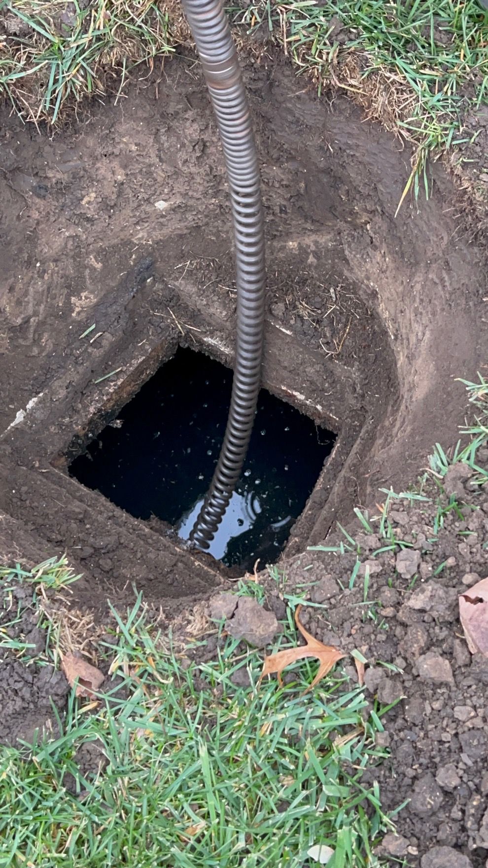 Man installing pipe into sewer. Orange gloves, open manhole, metal grate, truck in background.