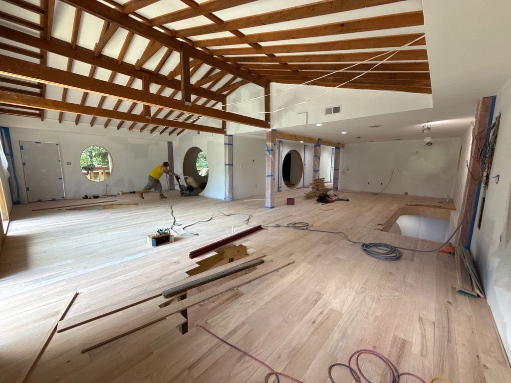 Renovated interior with exposed wooden beams, workers, and construction materials scattered across the floor