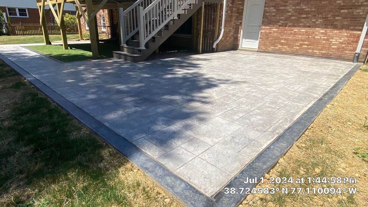 Concrete patio beside brick house with stairs and a grassy lawn in sunlight
