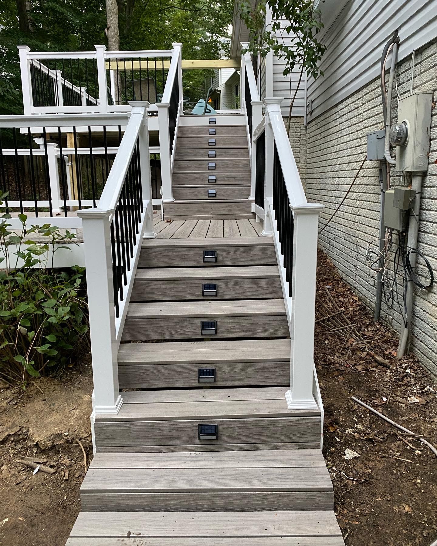 Wooden outdoor staircase with white railings leading up to a deck beside a house.
