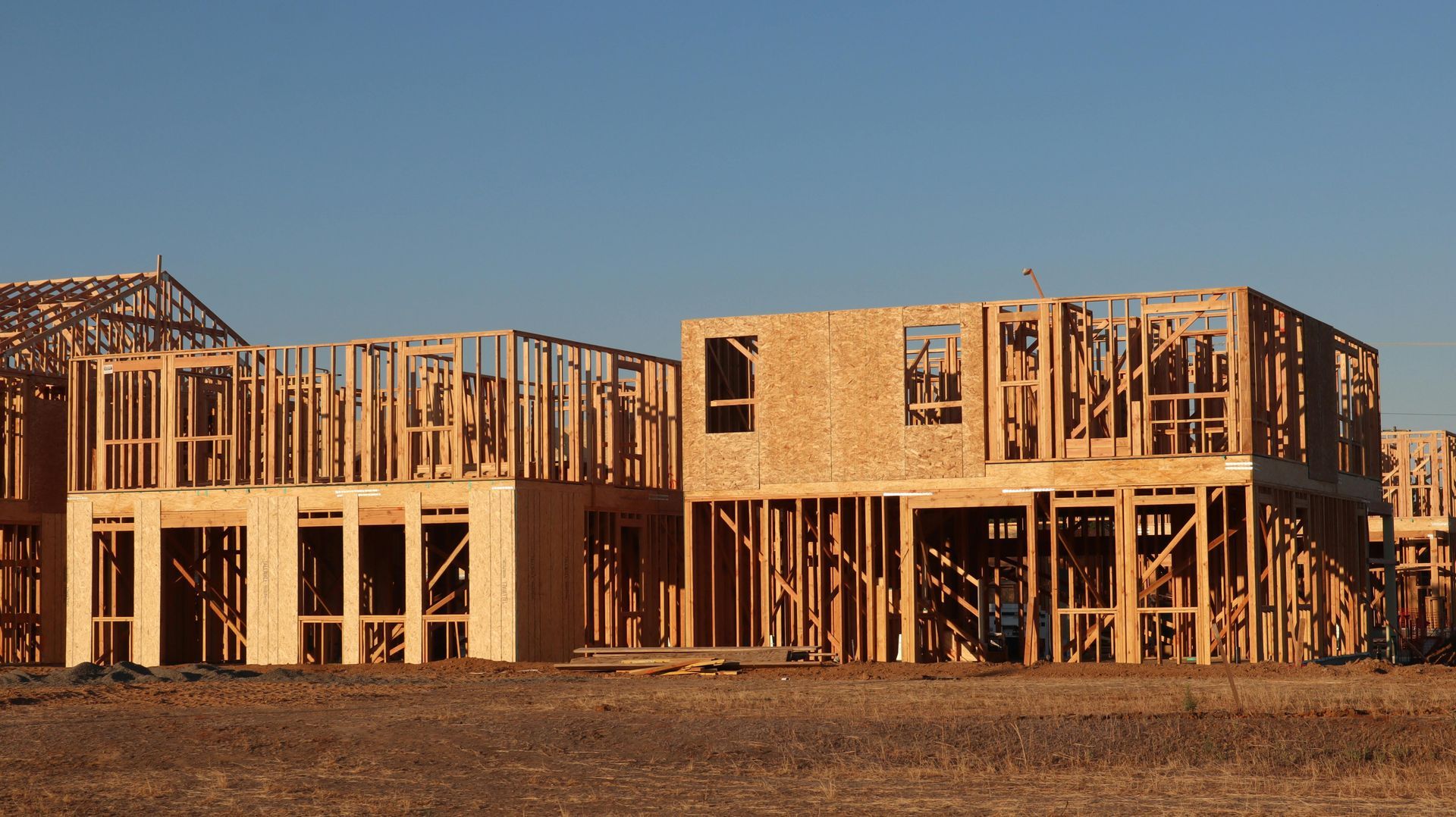 Two unfinished wooden house frames at sunset on a barren lot