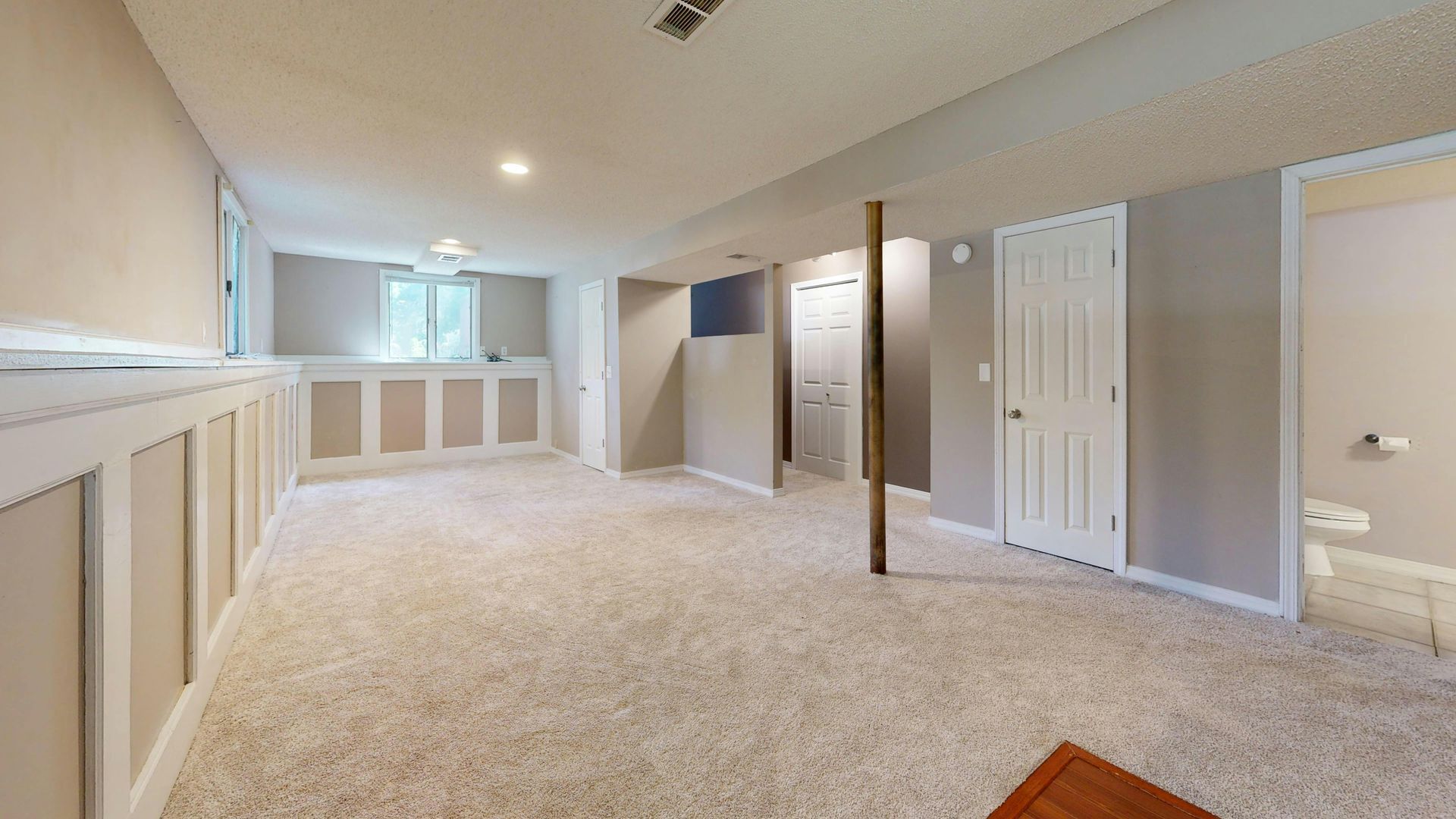 Empty beige carpeted room with vaulted ceiling, white trim, and closet doors
