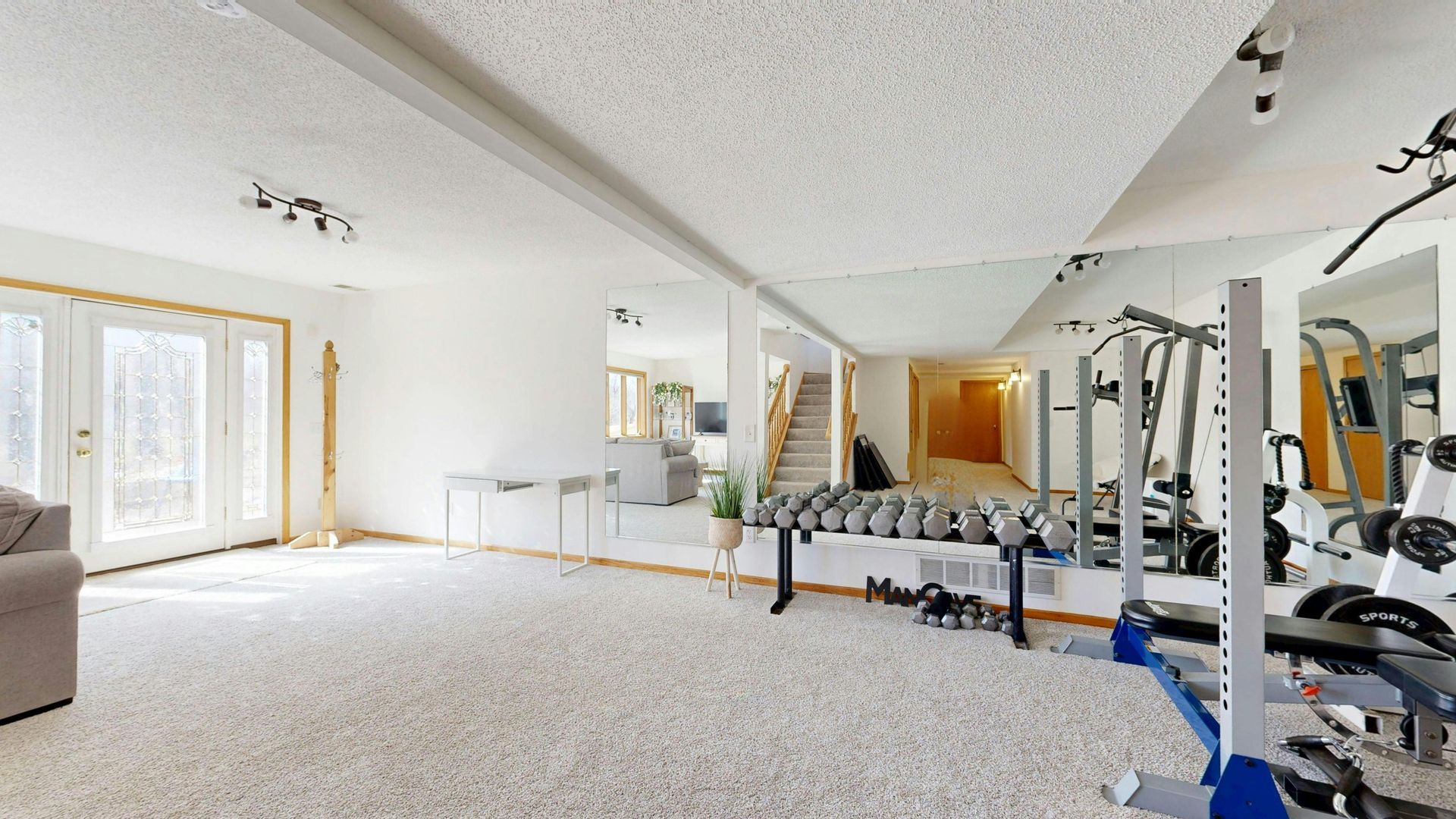 Bright home gym with weight bench, dumbbells, exercise machine, and sliding glass doors to outside