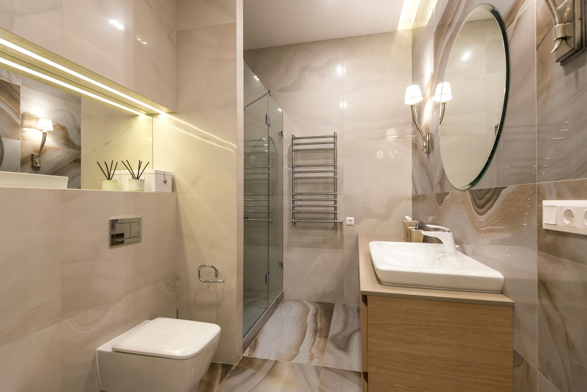 Modern beige bathroom with toilet, sink, shower, and large round mirror
