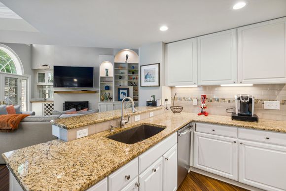 Bright kitchen with white cabinets, granite countertops, and a central island opening to a living room.