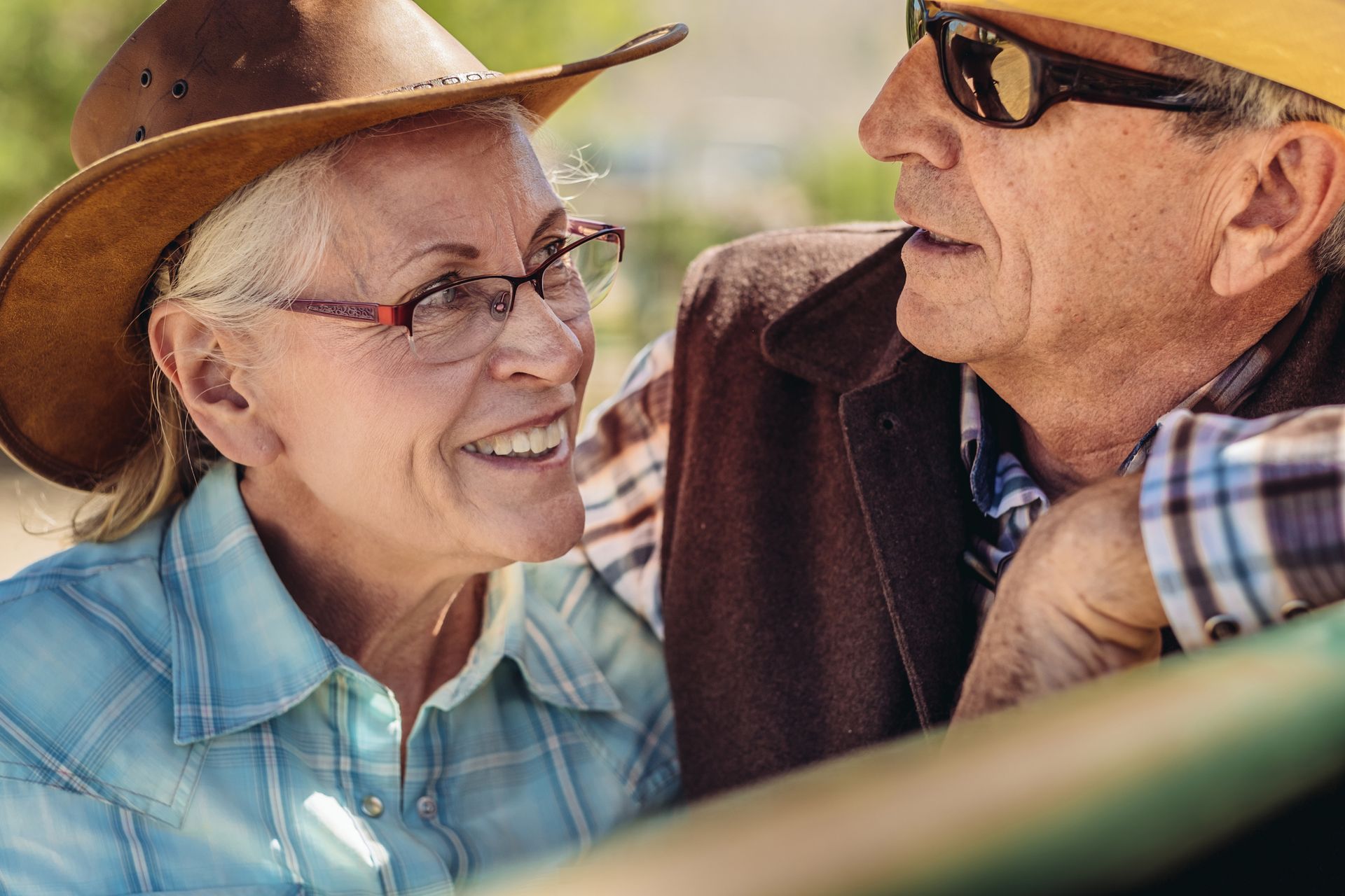 Two smiling people in cowboy hats talking outdoors in warm sunlight