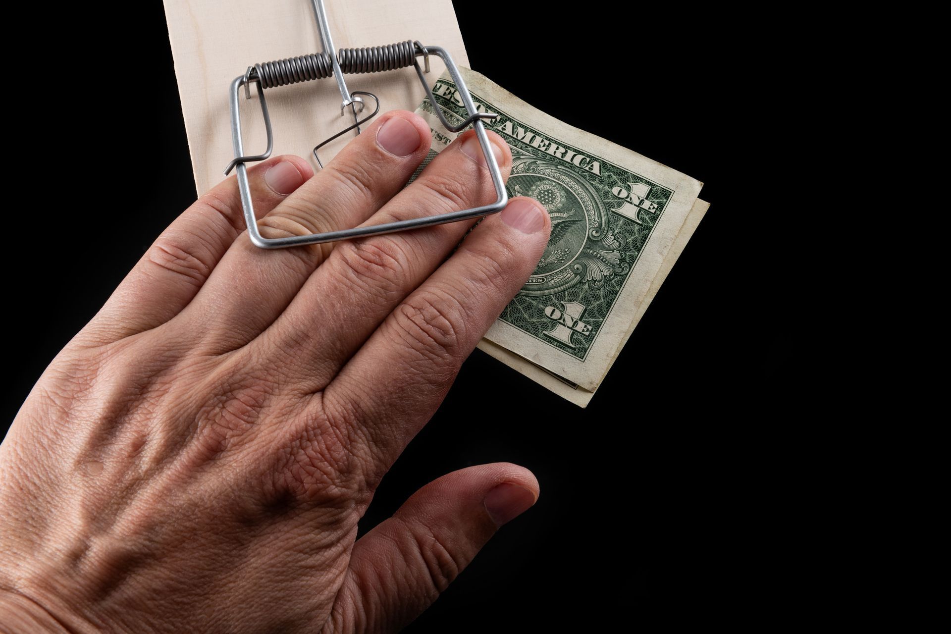 Hand placing a mousetrap over a U.S. dollar bill on a black background