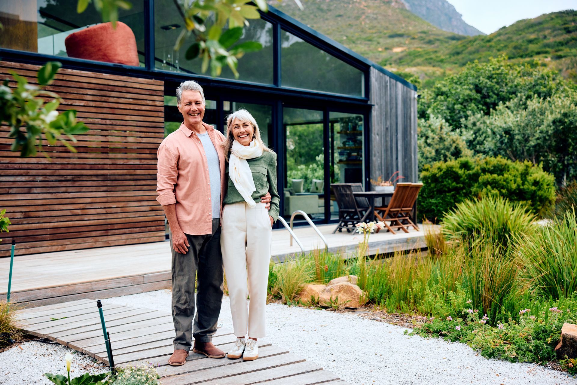 Couple standing on a patio outside a modern house with mountains and greenery in the background