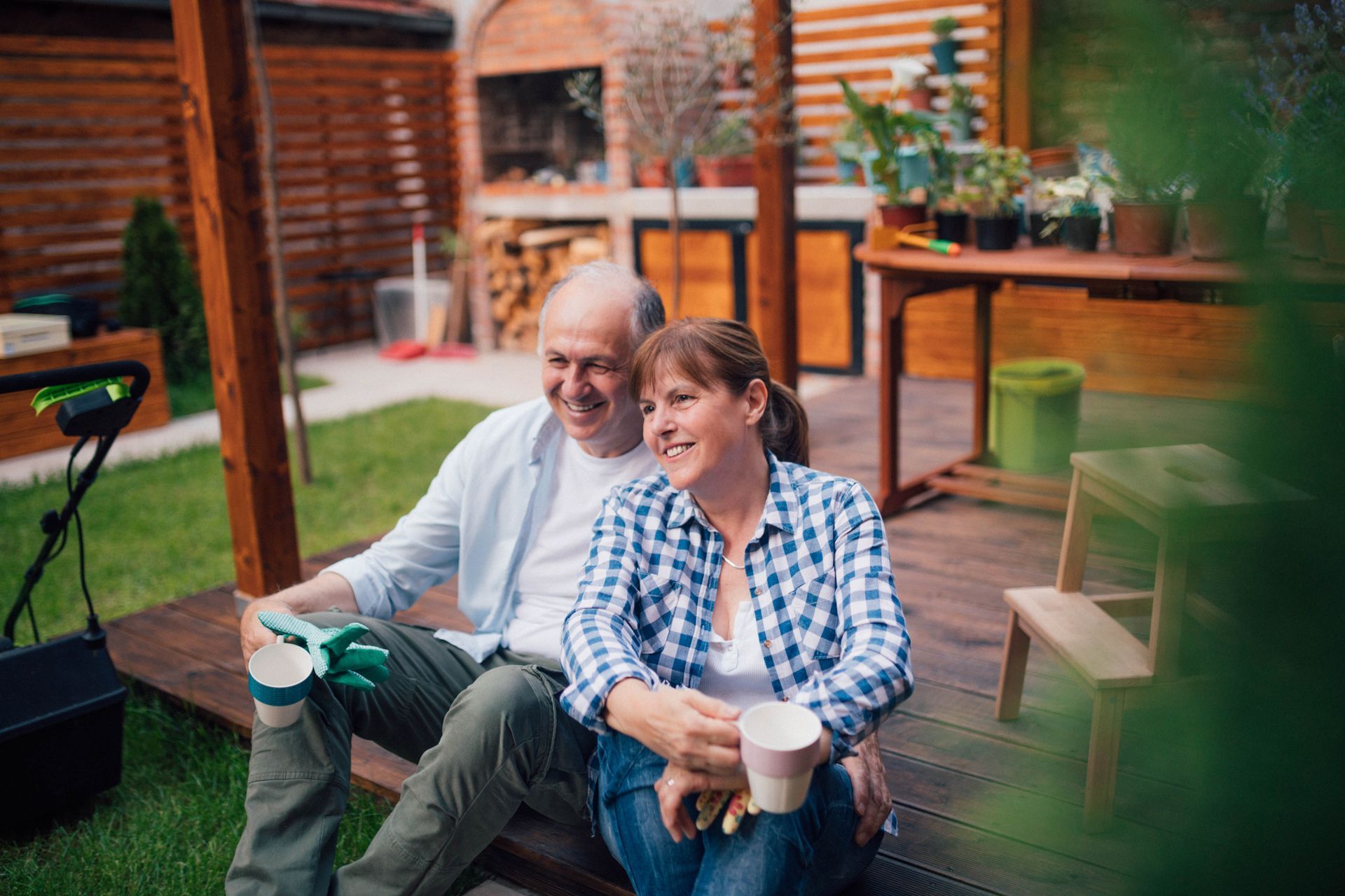 Two people sitting outdoors on a deck, smiling and holding drinks in a backyard.