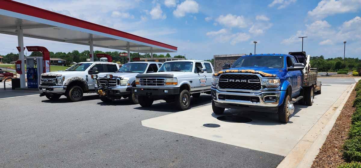 Four pickup trucks parked at a gas station under a red and white canopy on a sunny day.