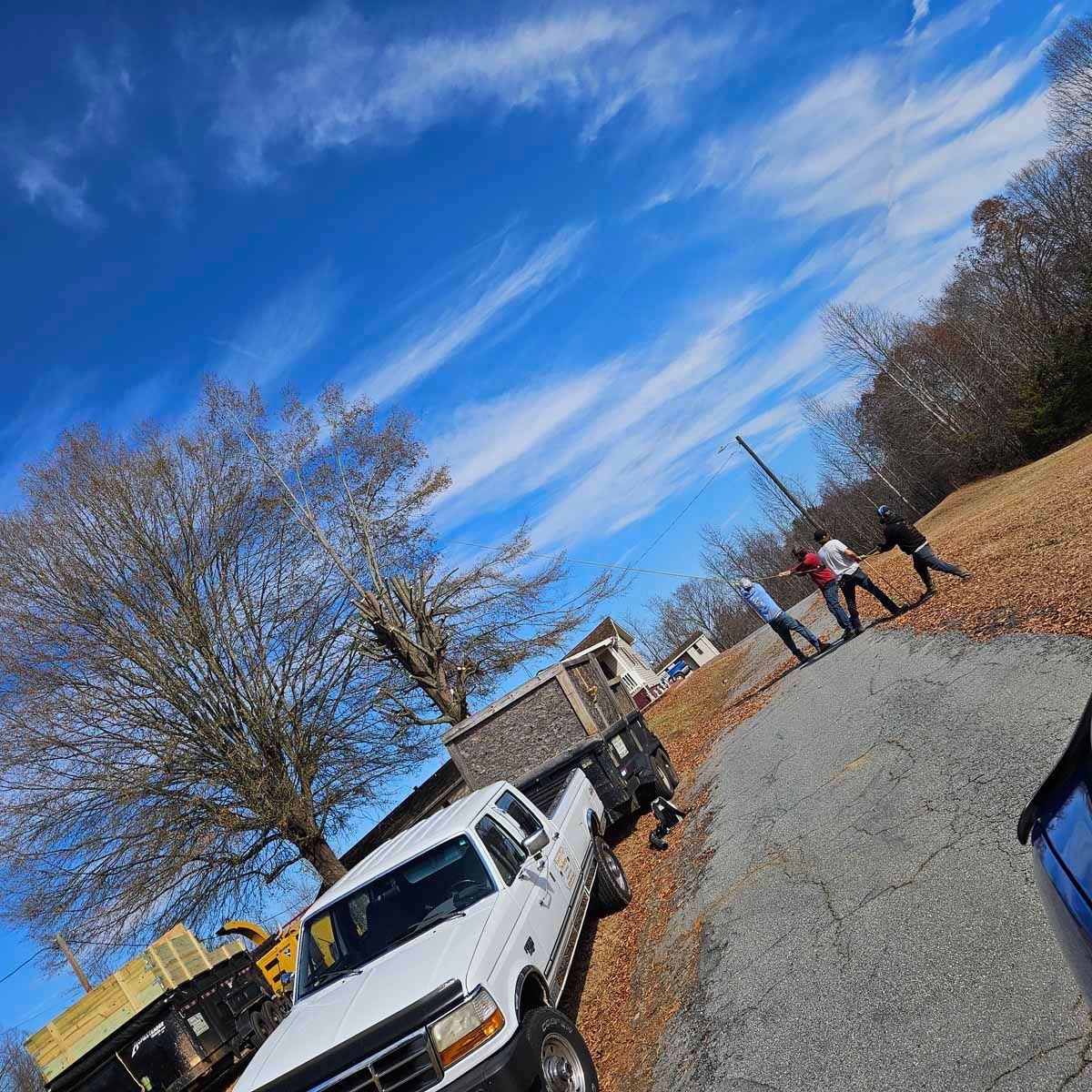 White truck parked on a gravel road, three people interacting on the right, blue sky with clouds.