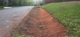 A dirt-lined roadside ditch next to a paved road and a grassy hill.