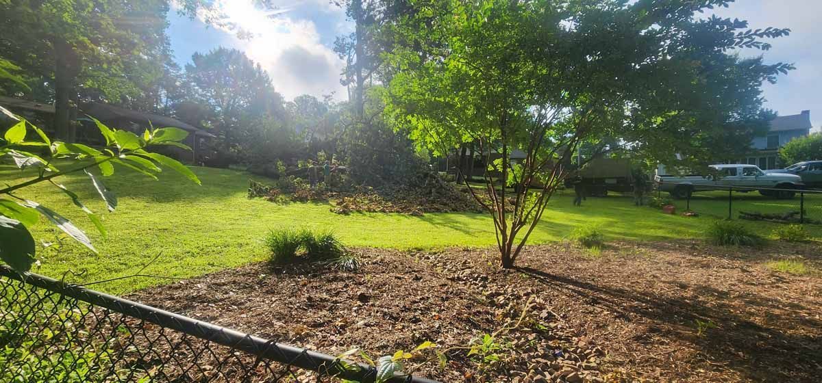 Lush green field with trees and gravel, sunlight peeking through clouds.