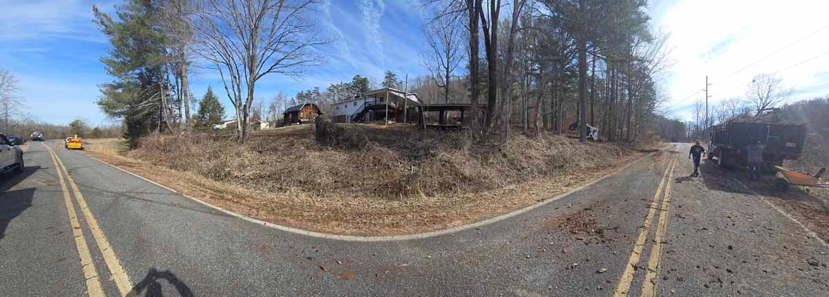 Curving road through a wooded area with a house and two people walking. Blue sky.