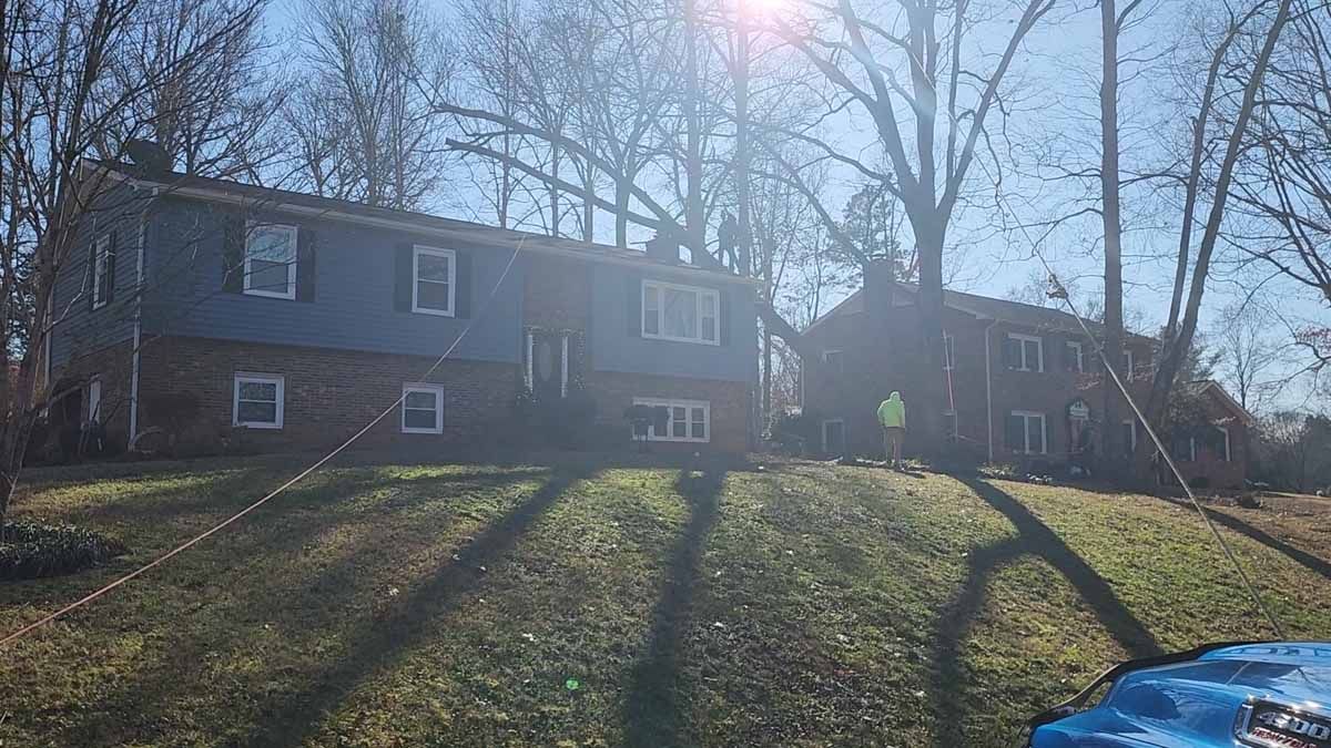 Two-story brick and siding houses on a grassy hill, trees in the background, bright sunlight.