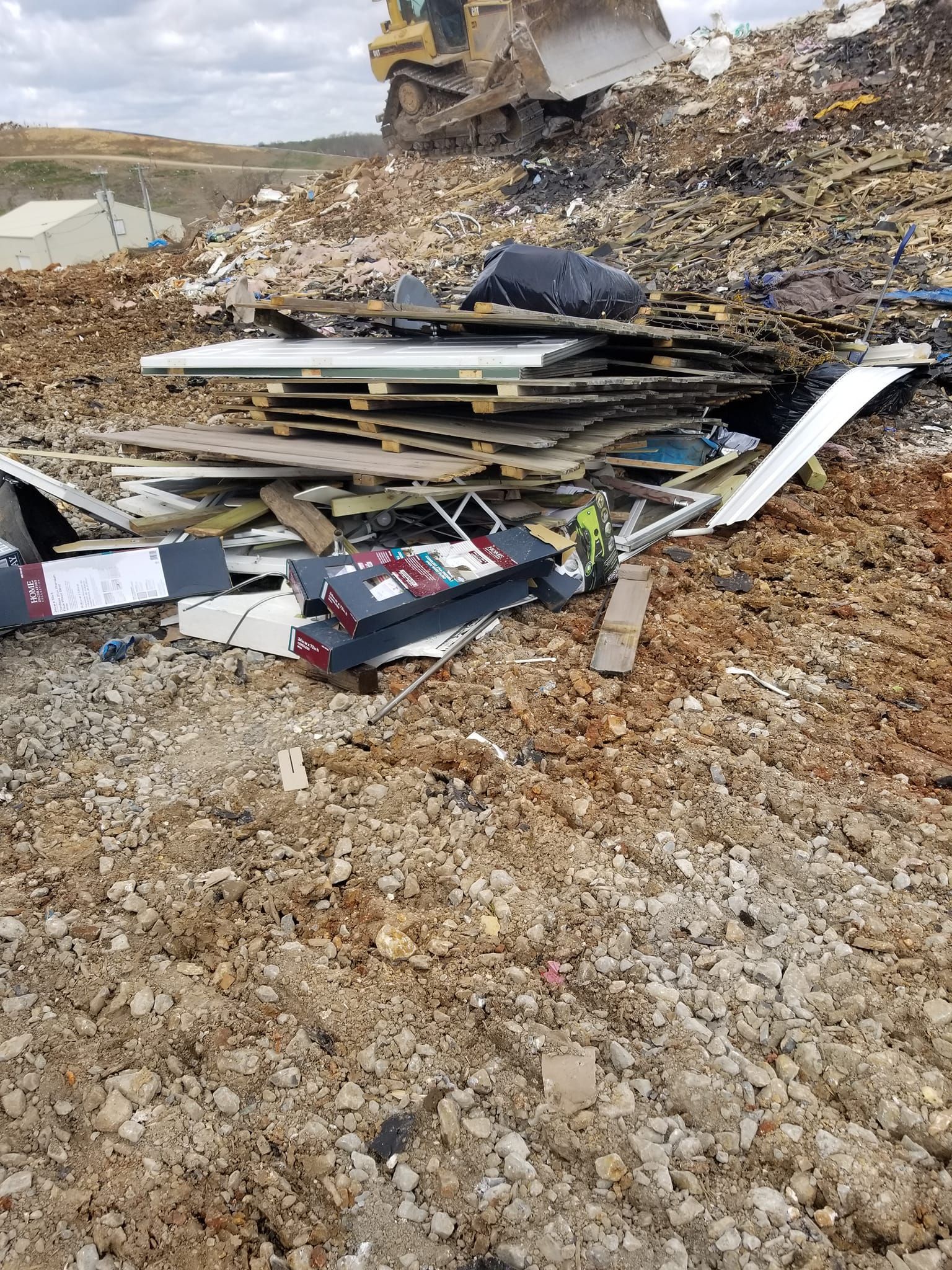 Bulldozer pushes debris on a landfill. Wood, metal, and construction materials mixed. Overcast sky.