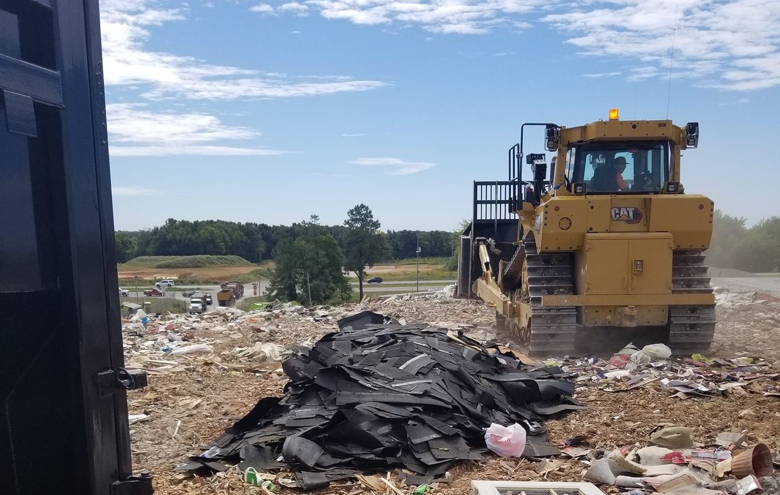Landfill with a bulldozer compacting trash under a blue sky.