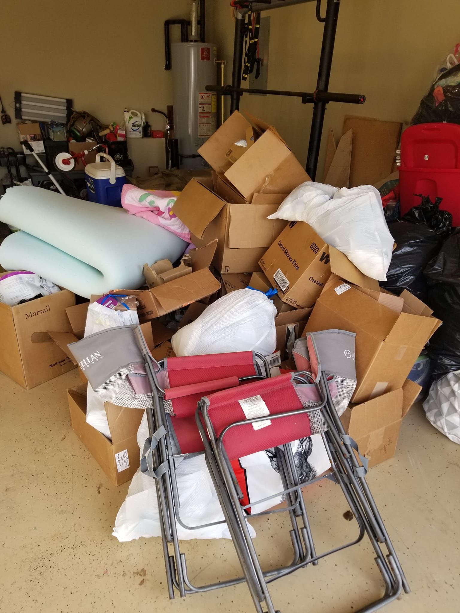 Cluttered garage with cardboard boxes, folding chairs, and bags.