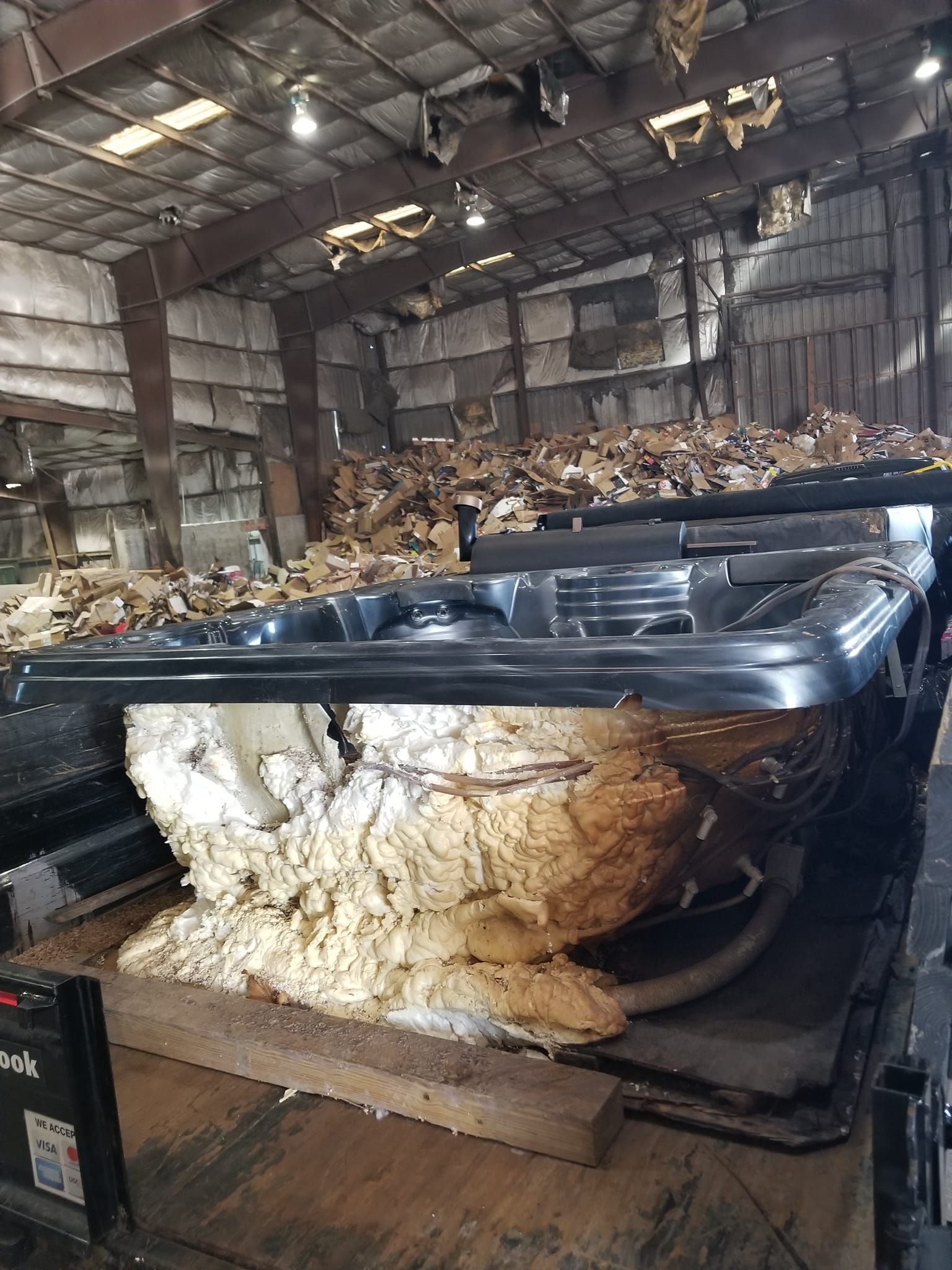 A dismantled black hot tub in a warehouse filled with debris.  Foam insulation is exposed.