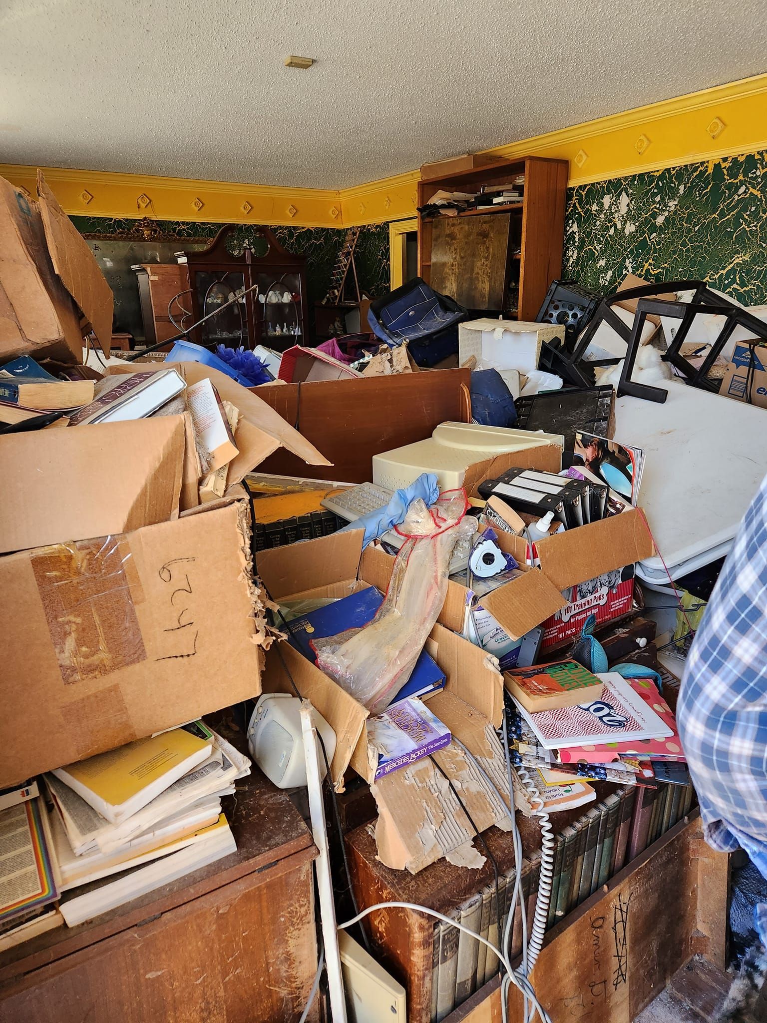 A cluttered room with cardboard boxes, furniture, and various items, indicating disorganization.