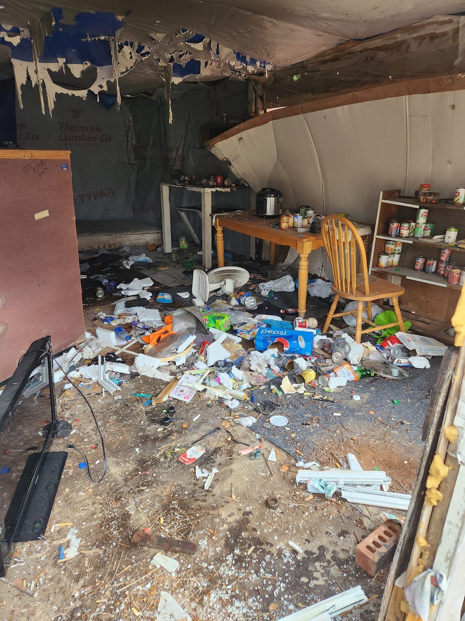 Messy room with debris, damaged walls, and a table. Toys and items scattered on the floor.