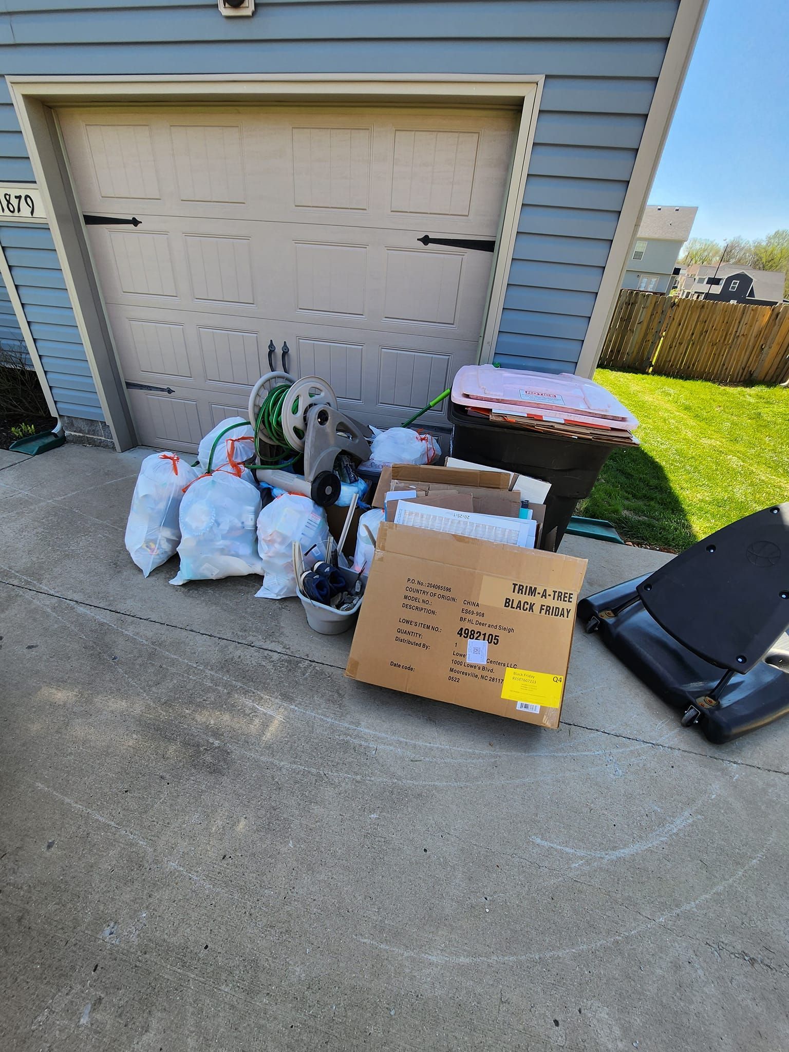 Pile of bags, boxes, and items sit on driveway in front of a garage.