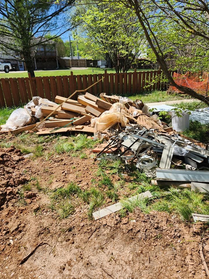 Pile of construction debris, including wood and metal, on grass in a yard near a wooden fence.