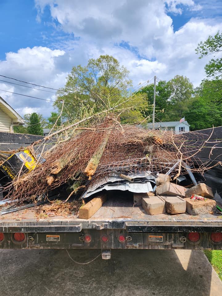A truck bed overflowing with debris, including tree branches, metal, and brick, under a cloudy sky.