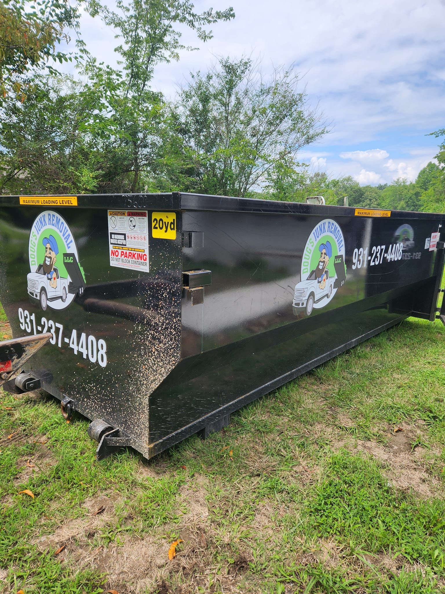 Black dumpster on green grass; company logo with phone number visible.