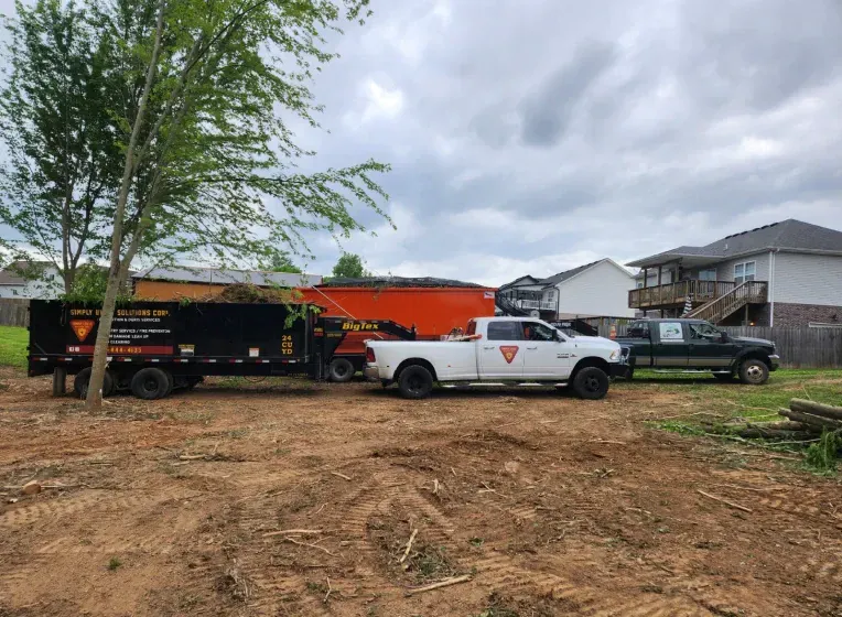 Two trucks and a trailer on a dirt lot, likely for landscaping or tree removal.