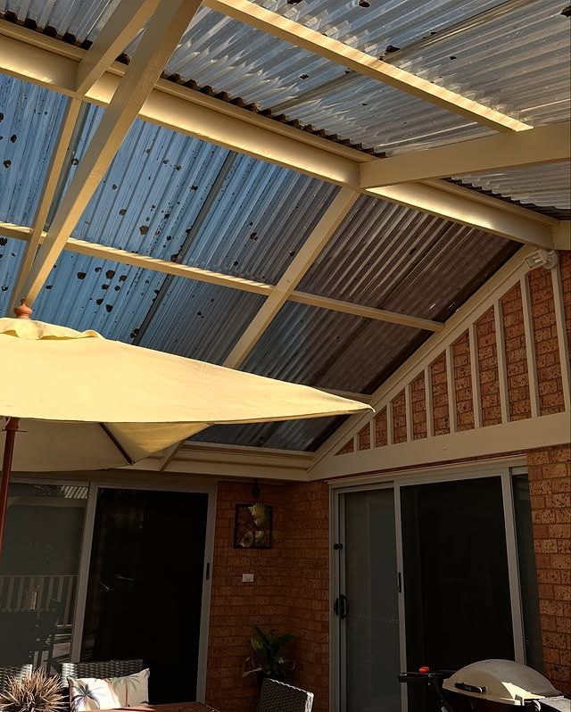 A patio with a corrugated translucent roof and a yellow umbrella. Brick wall and sliding glass doors are visible.
