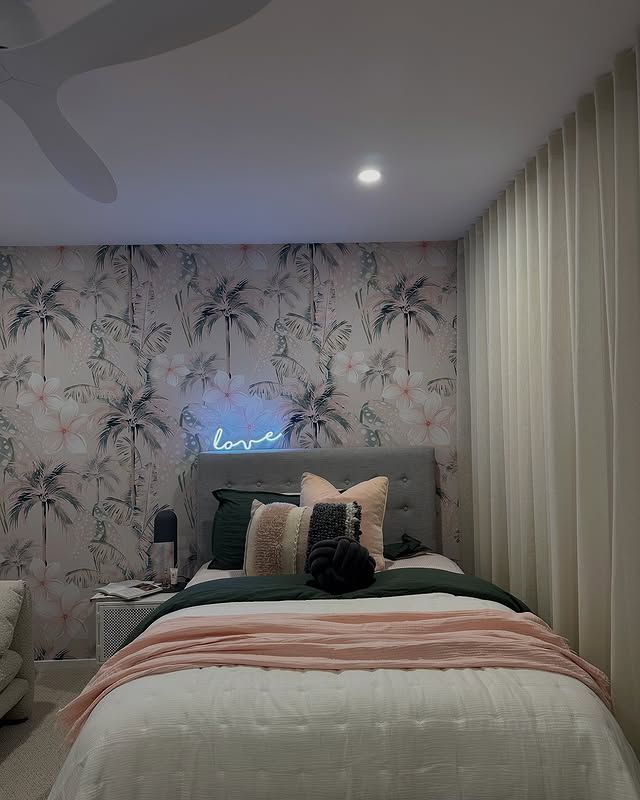 A bedroom with palm tree wallpaper, a bed with pink and green bedding, and a neon 