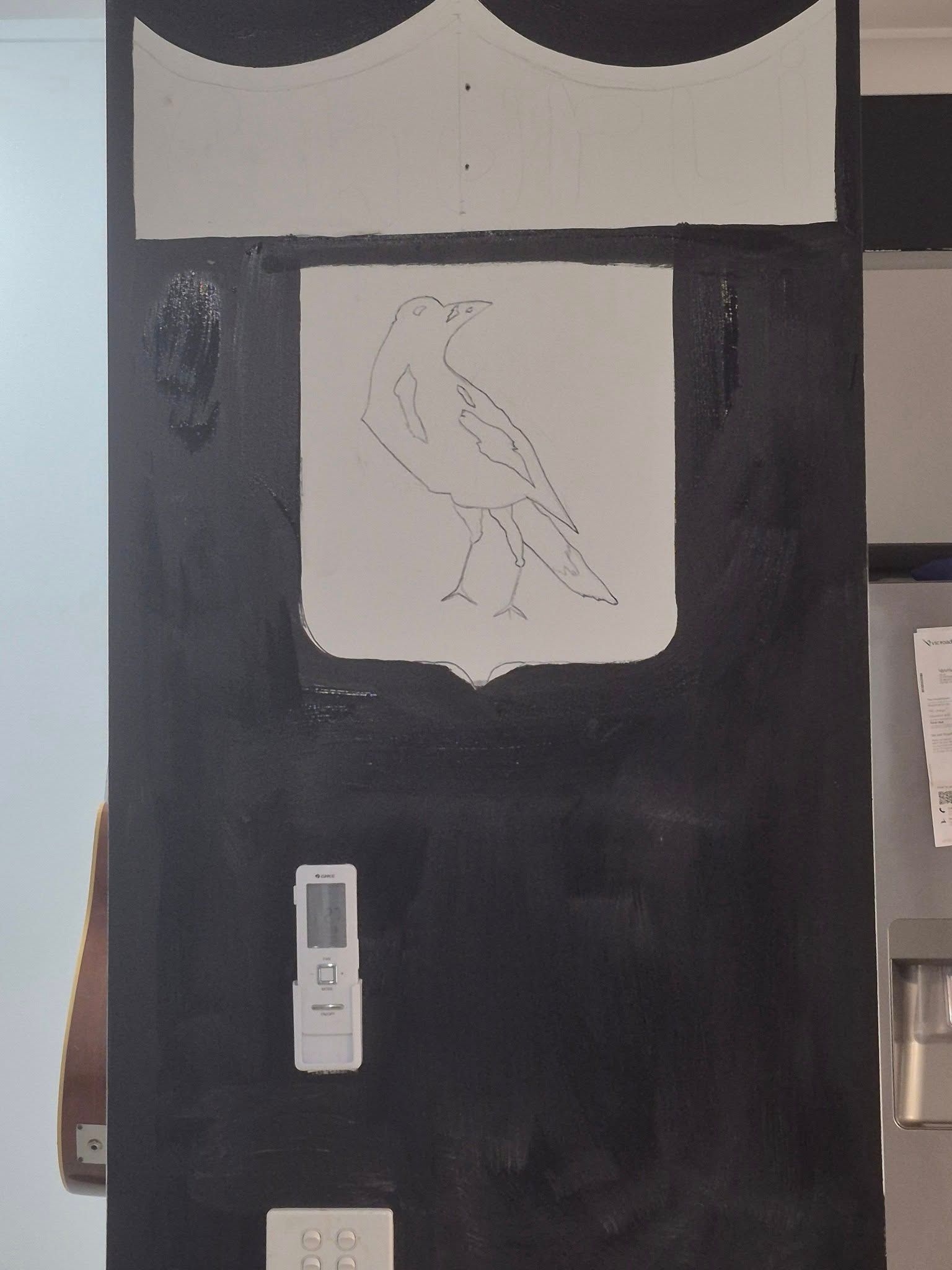 Black painted wall with a white bird drawing on a shield, a remote control, and a light switch.