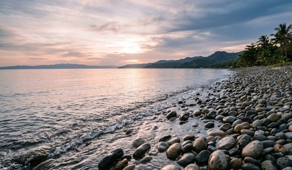 Rocky shoreline at sunset with calm water and distant hills near Milton, VT