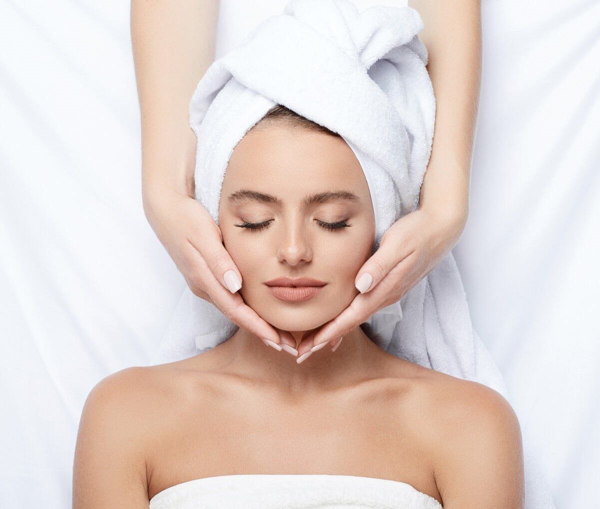 A woman with a towel wrapped around her head is getting a facial massage.