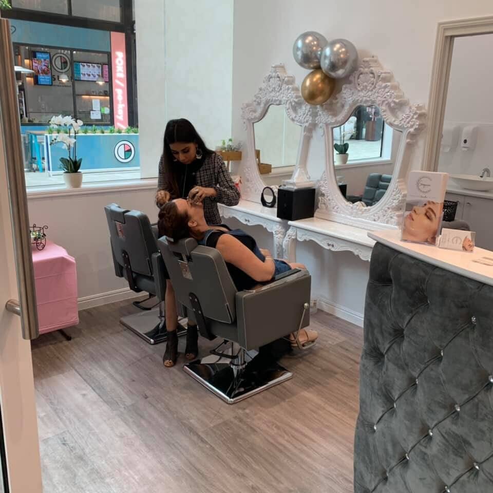 A woman is getting her makeup done in a salon while sitting in a chair.