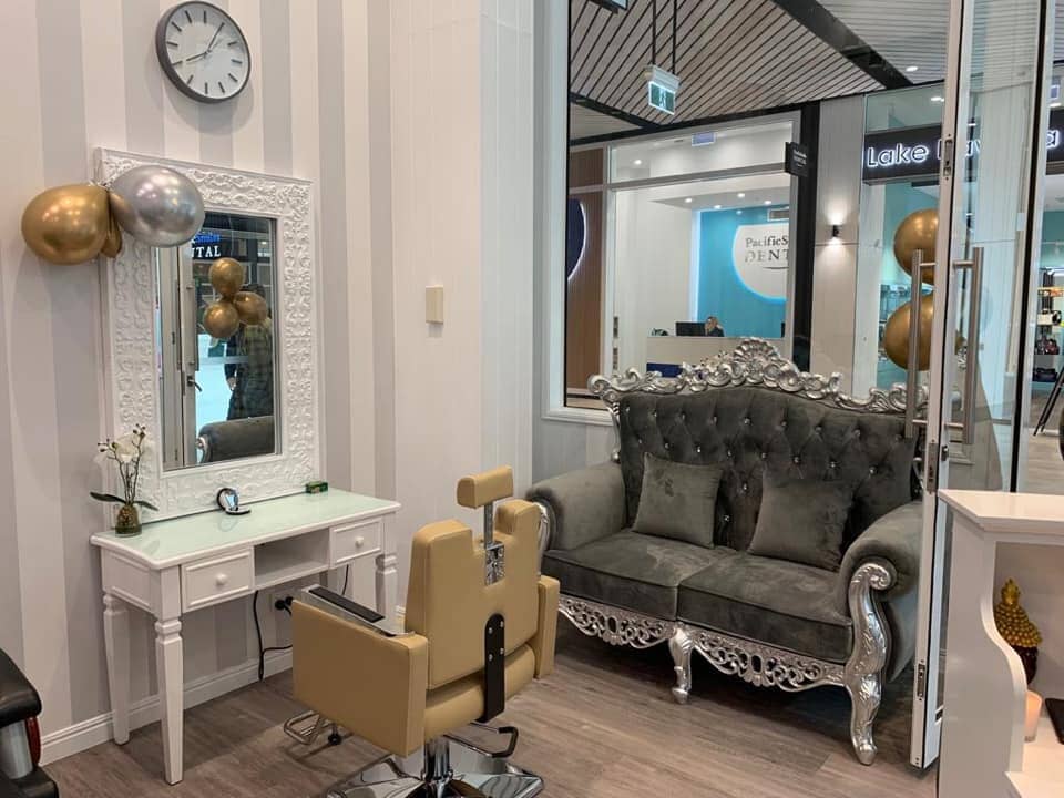 A salon with a couch , chair , mirror and clock.