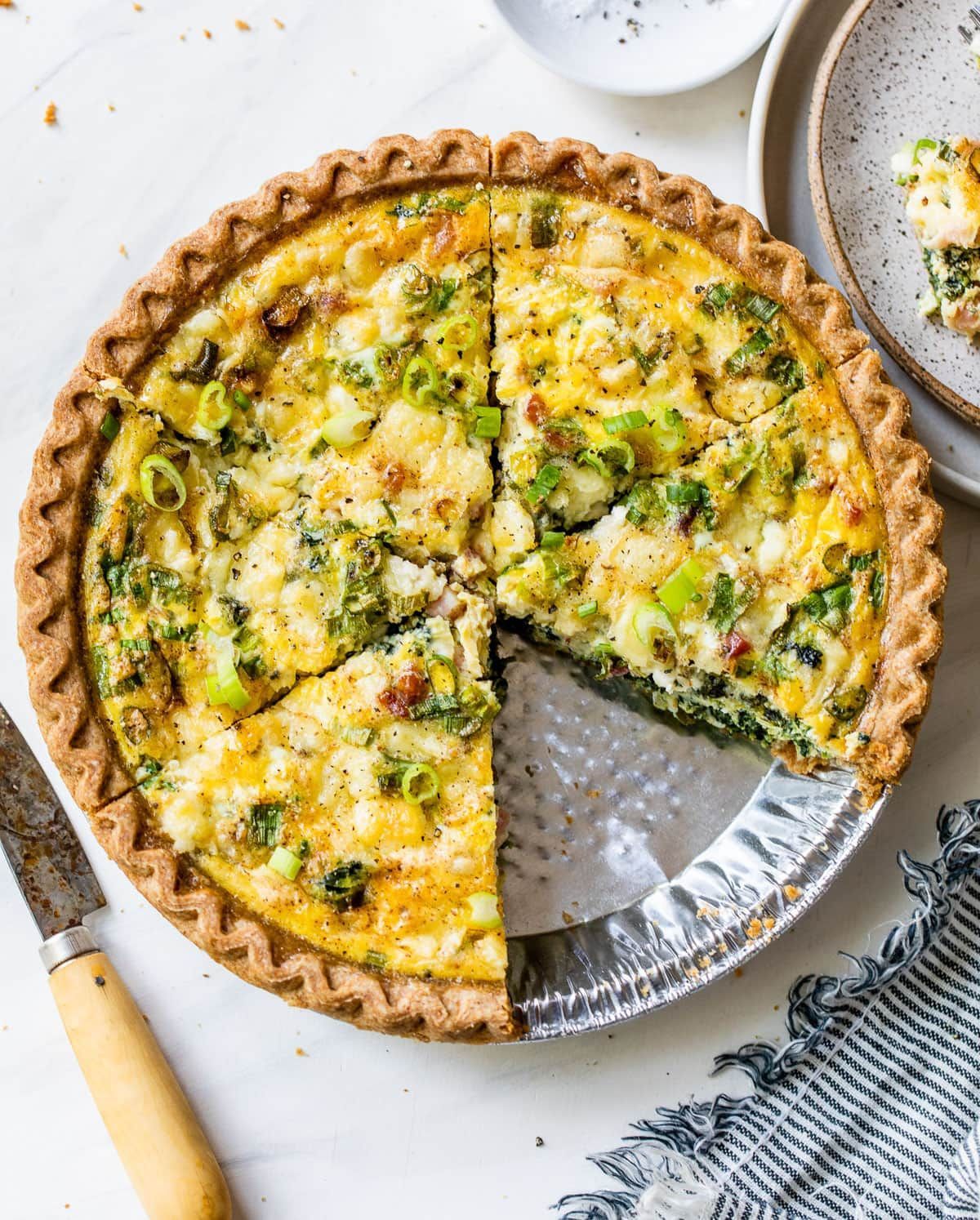 A quiche with a slice taken out of it is sitting on a table.