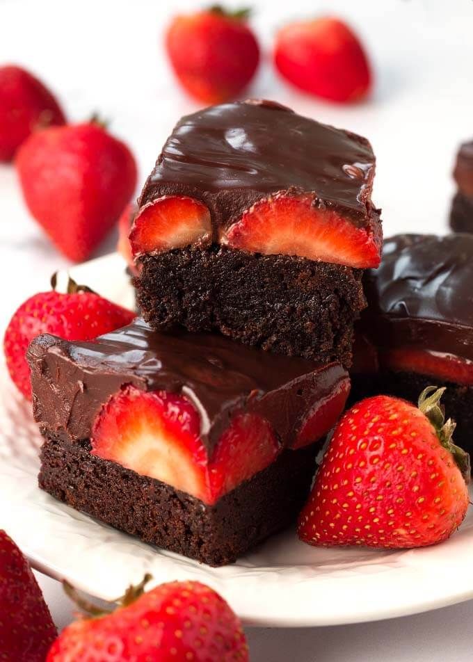 A white plate topped with chocolate brownies and strawberries