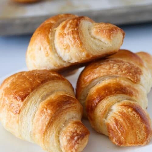 Three croissants are stacked on top of each other on a white plate.