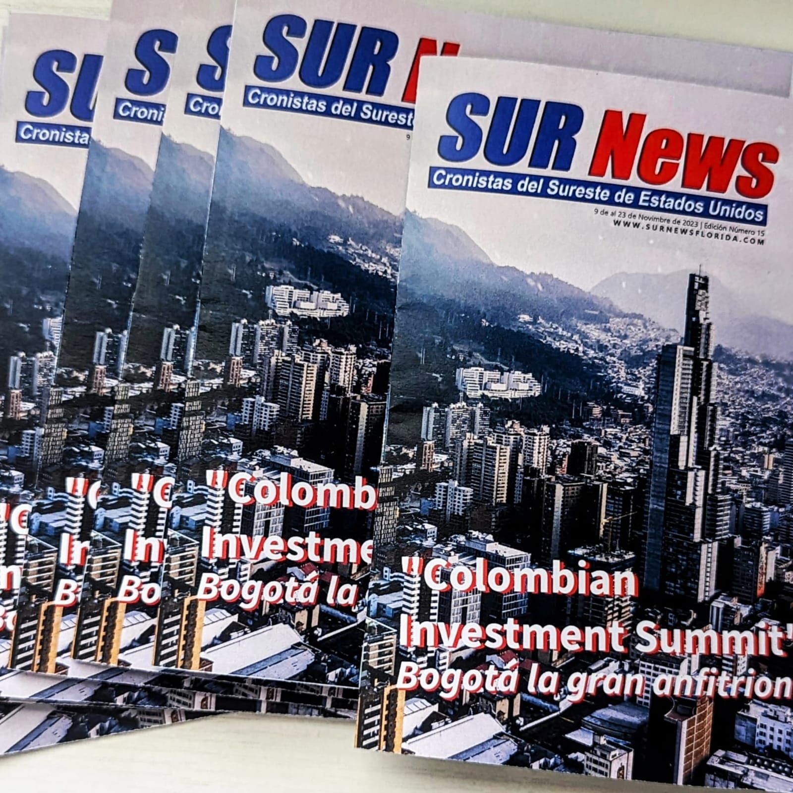 Stack of SUR News magazines with a cityscape on the cover. The headline is "Colombian Investment Summit" in Bogotá, Colombia.