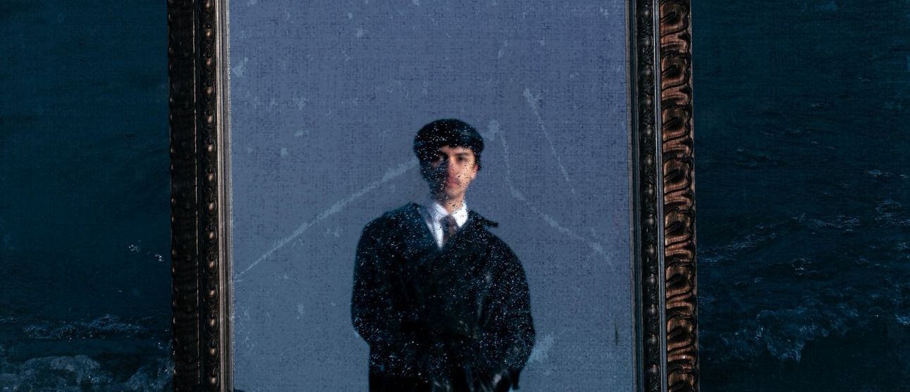 A person in a suit appears in a large ornate mirror, against a blue background. The reflection appears misty, as if underwater.