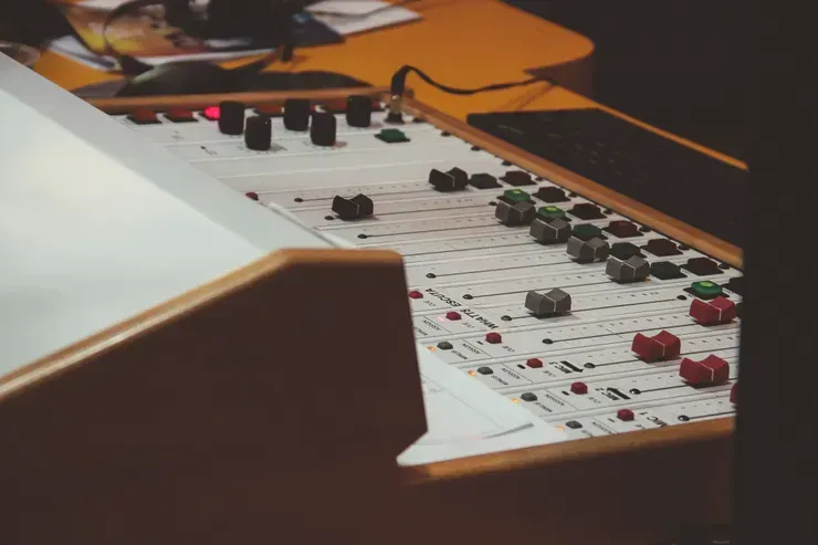 Close-up of a sound mixing board with knobs and sliders, lit by warm light.