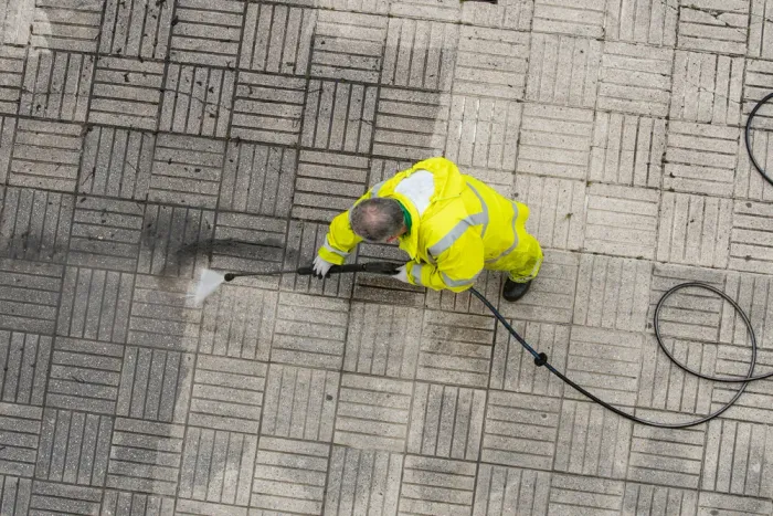 A man in a yellow suit is cleaning a tiled floor with a high pressure washer.