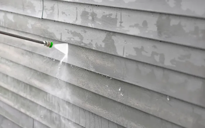 A person is cleaning the side of a house with a high pressure washer.