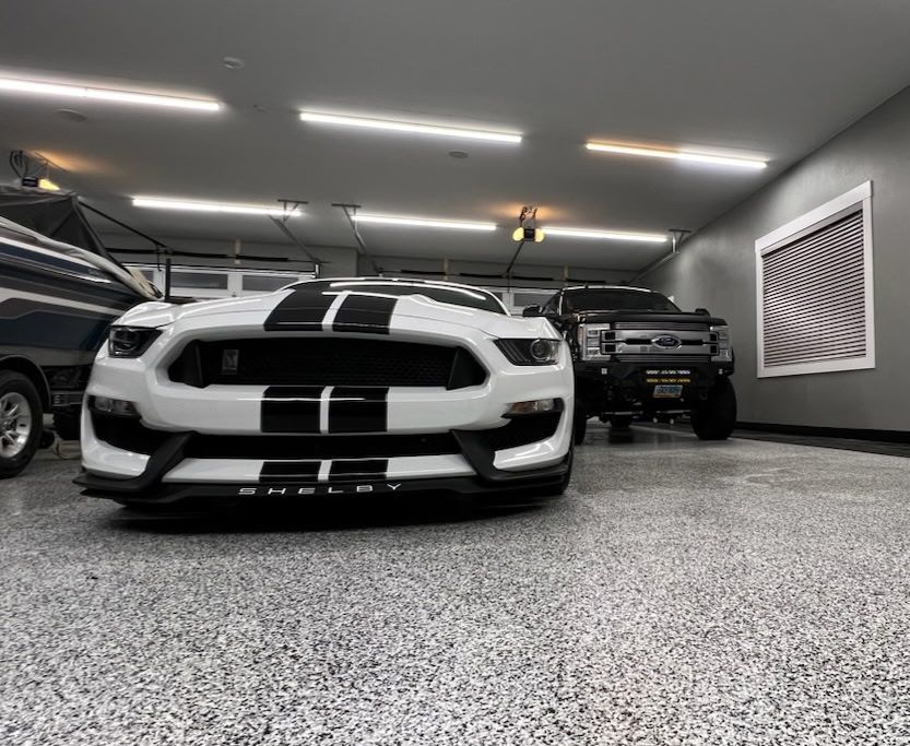 A white car is parked in a garage next to a truck.