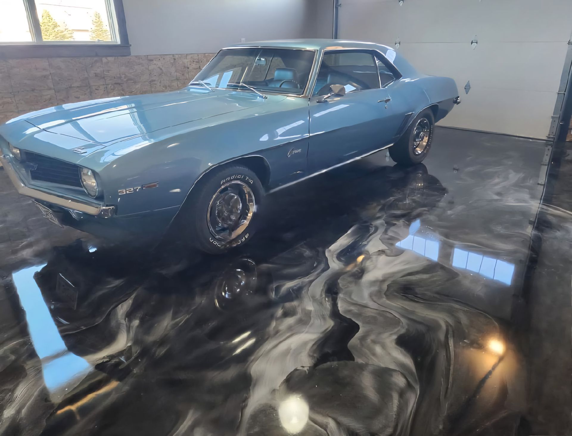 A blue car is parked on a black and white epoxy floor in a garage.