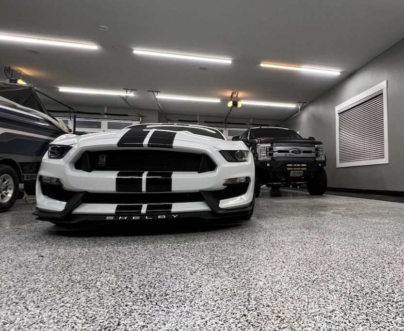 A white car is parked in a garage next to a black truck.