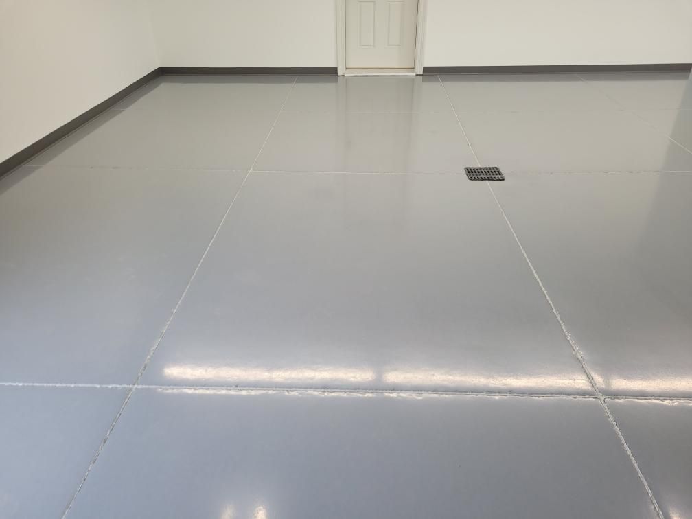 A gray tiled floor in a garage with a door in the background.