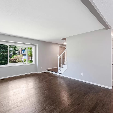 An empty living room with hardwood floors and a large window.